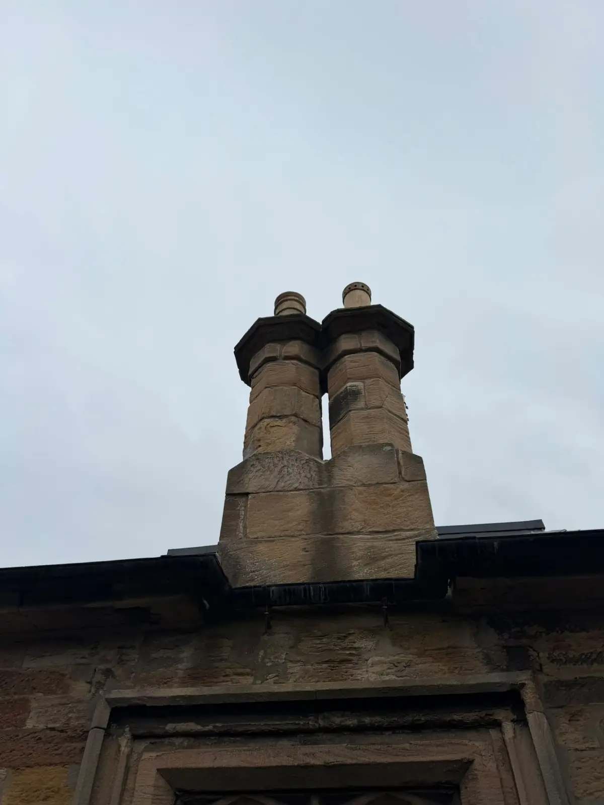 Repointed sandstone chimney stack with lead work along the roof edge